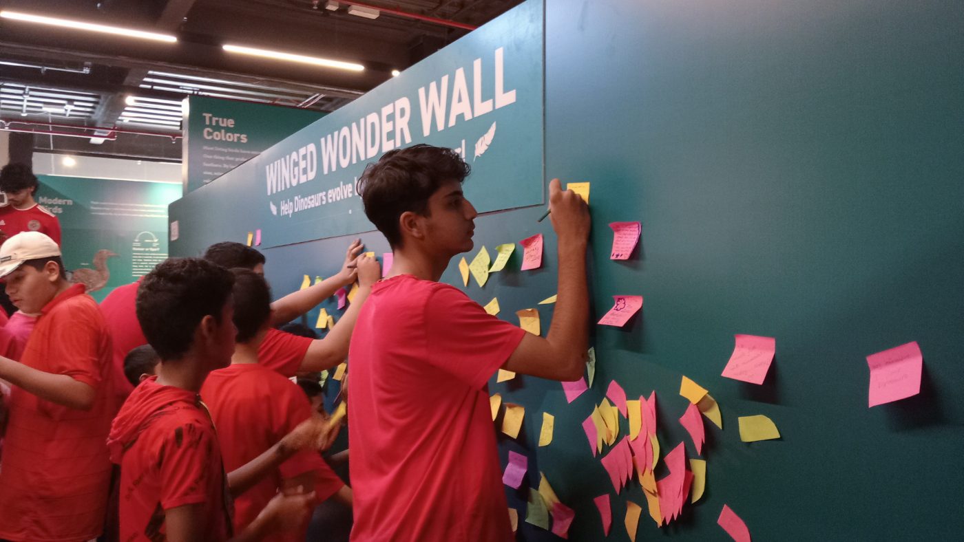 Students writing on sticky notes and adding them to the Winged Wonder Wall