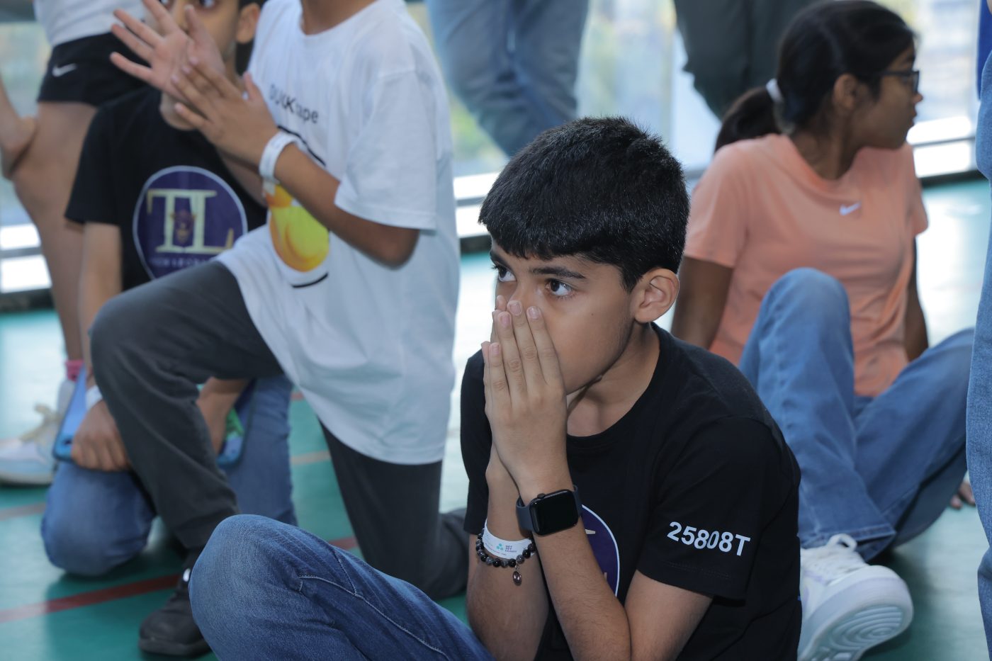 A student sitting at the field edge with his hands over his mouth, watching a match