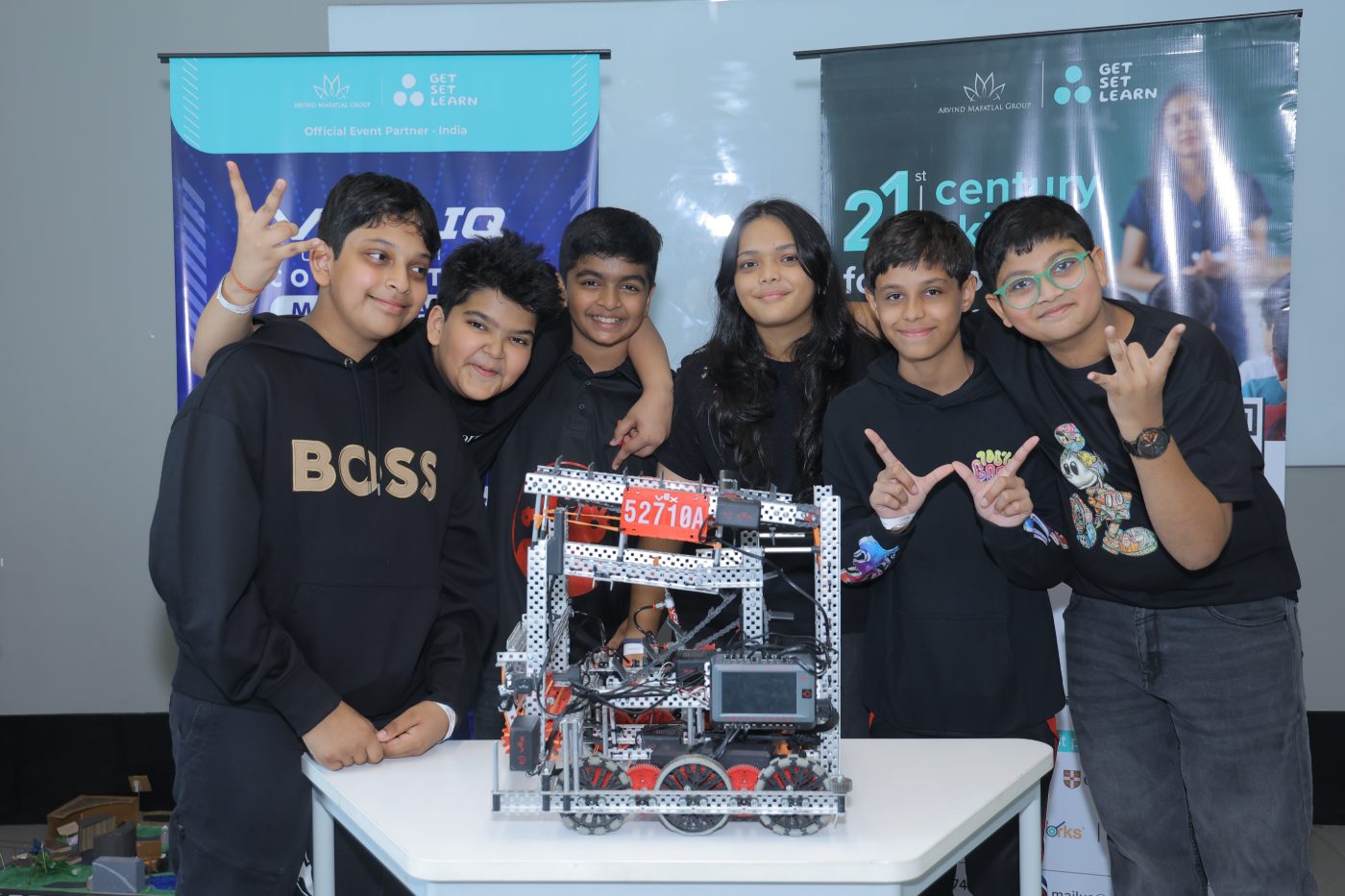 Six students standing with their VEX IQ robot in front of the Get Set Learn event banners