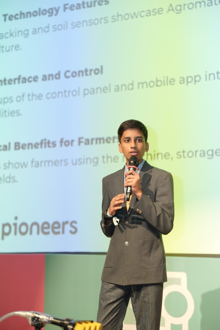 A student presenting a farming technology idea, with the technology features slide behind him